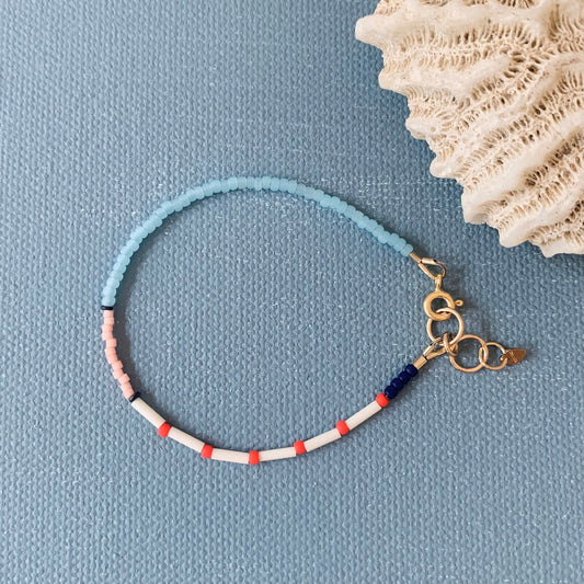 Bracelet with blue, white, and red beads on a blue background with coral.